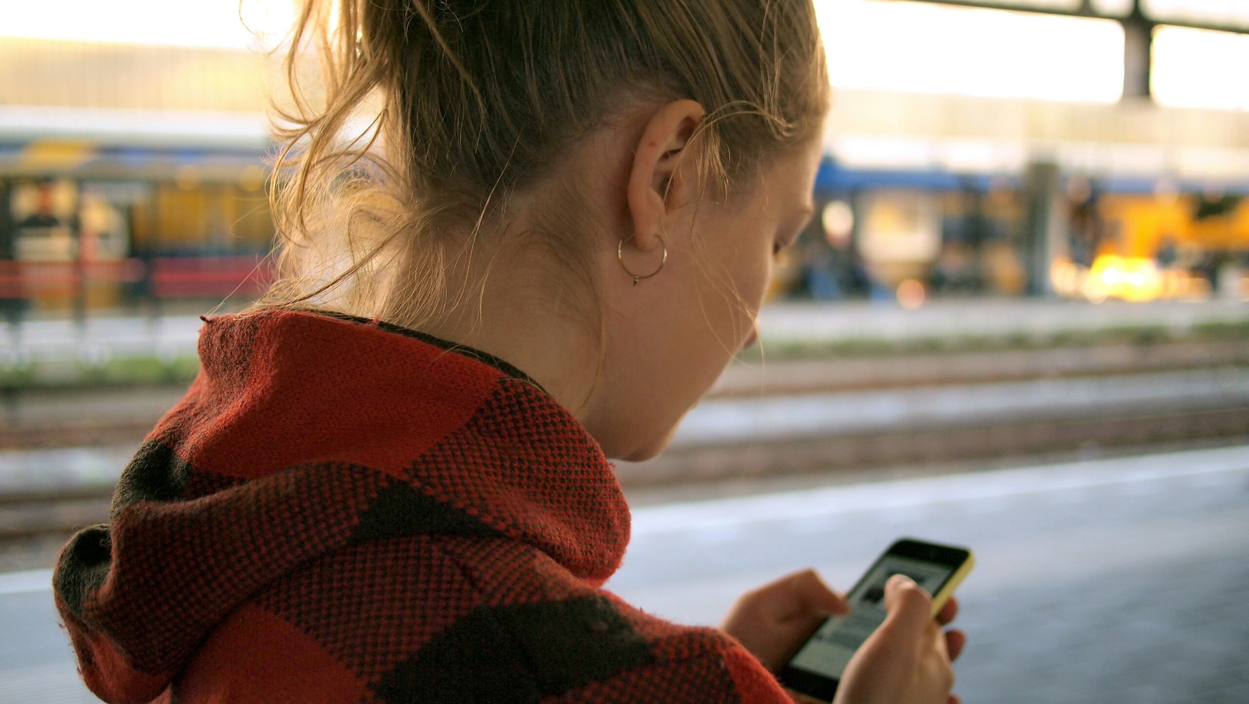 Woman looking at smartphone while walking on train platform.
