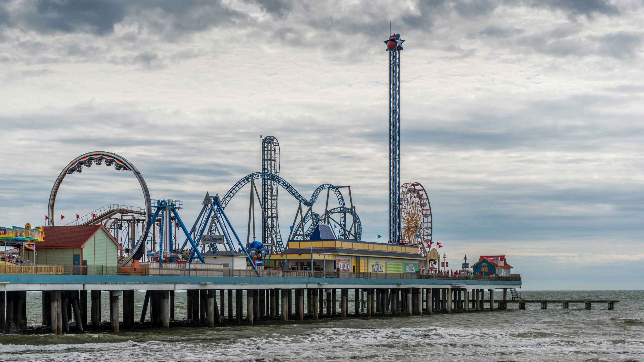 Pier with amusement park rides on it on cloudy day.