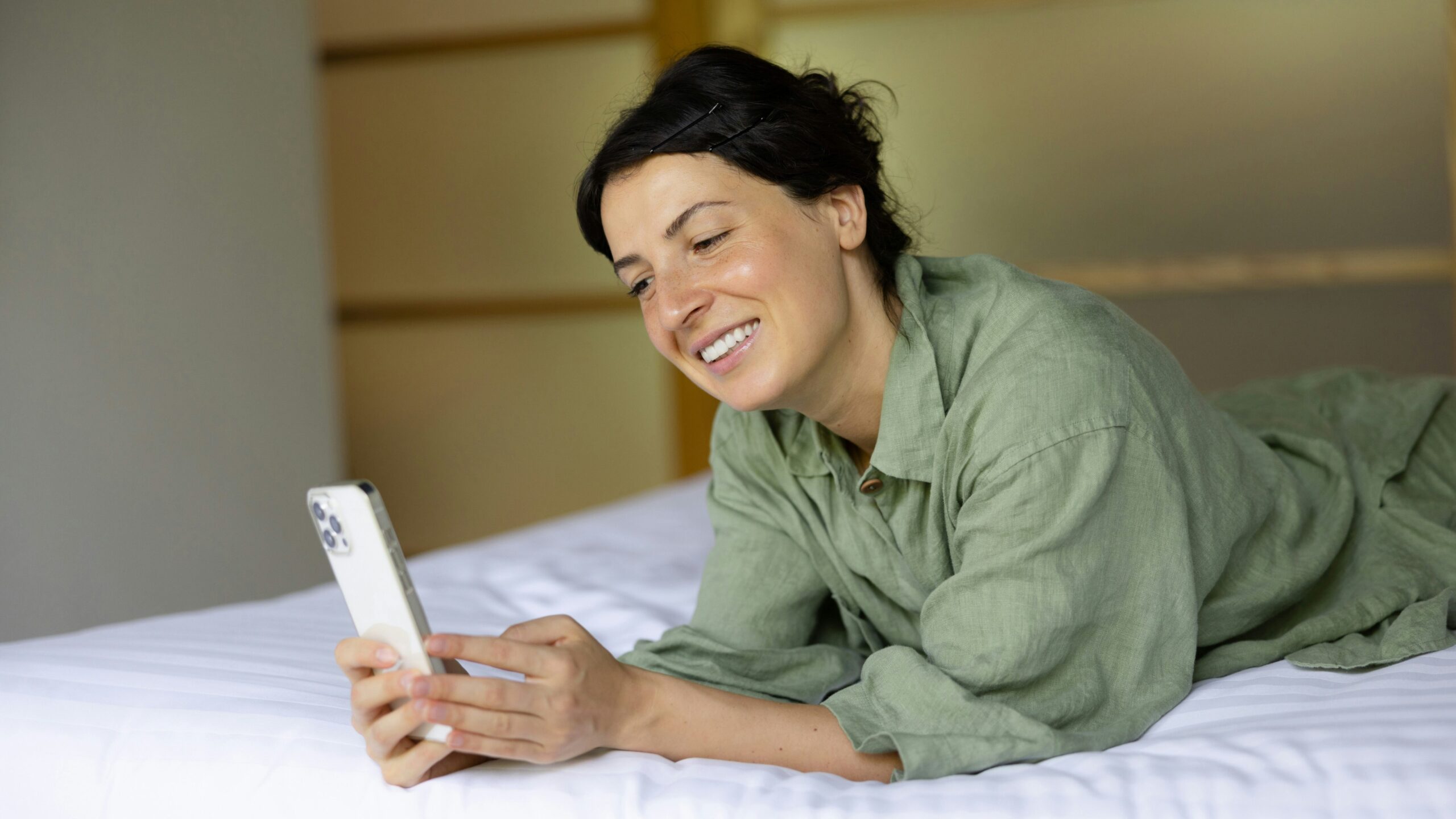 Mobile App | Krista the Explorer Woman lying on a bed, smiling at a smartphone in her hands.