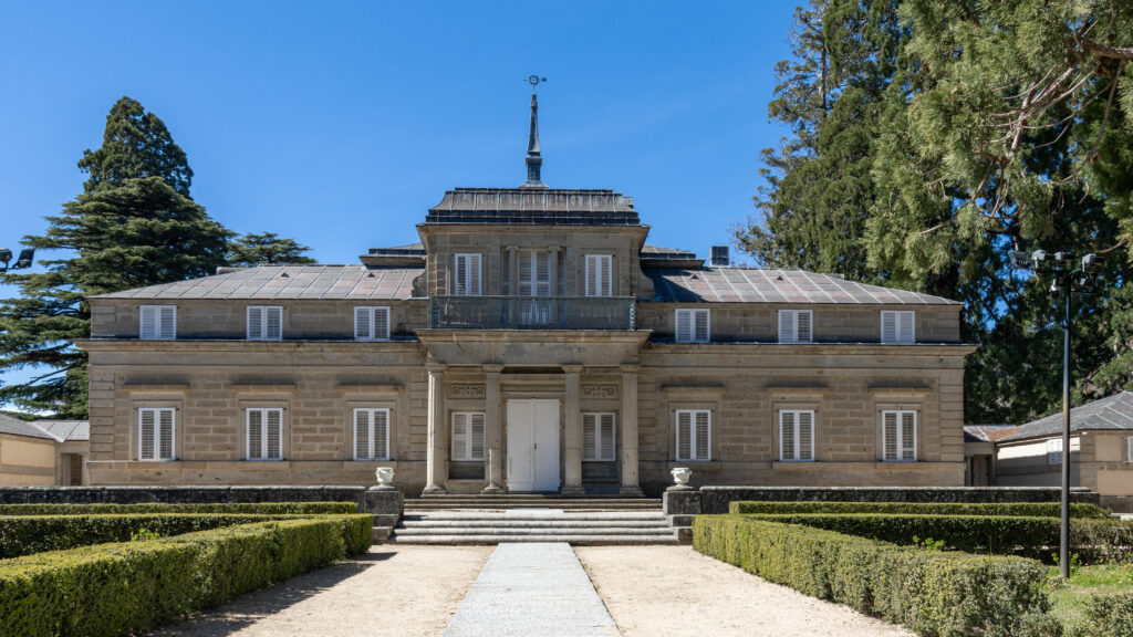 Stone mansion with a central doorway, white shutters, and a small balcony.