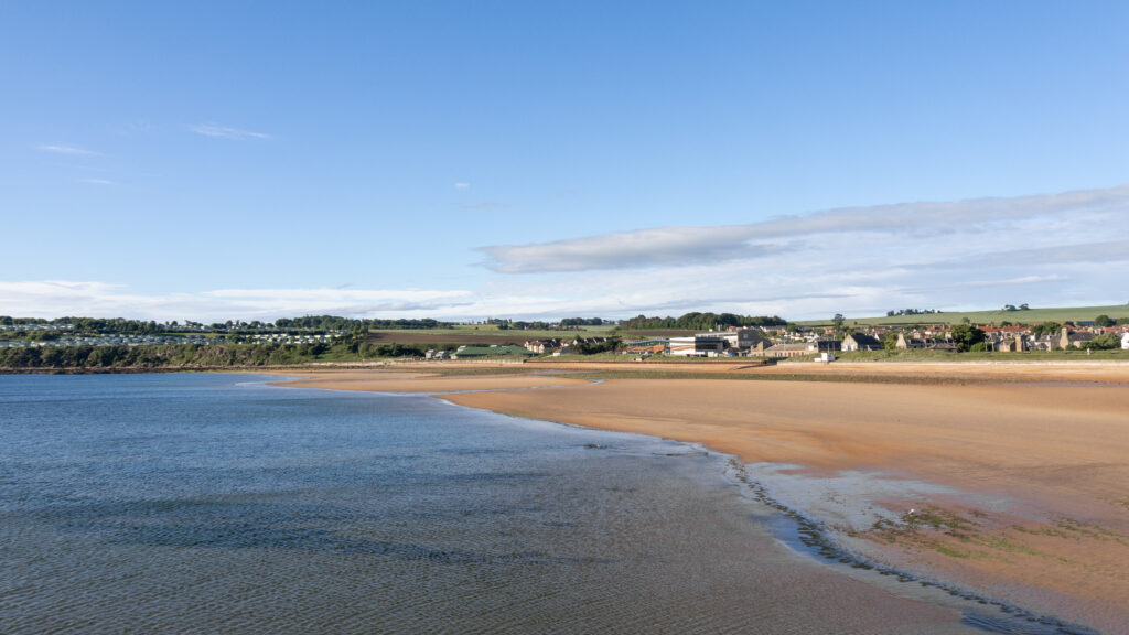 Coastal town along a sandy shore with calm, blue water.