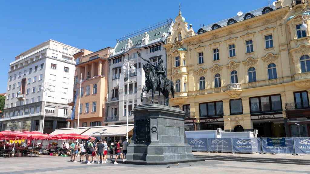 Equestrian statue in a busy city square with ornate pastel buildings.