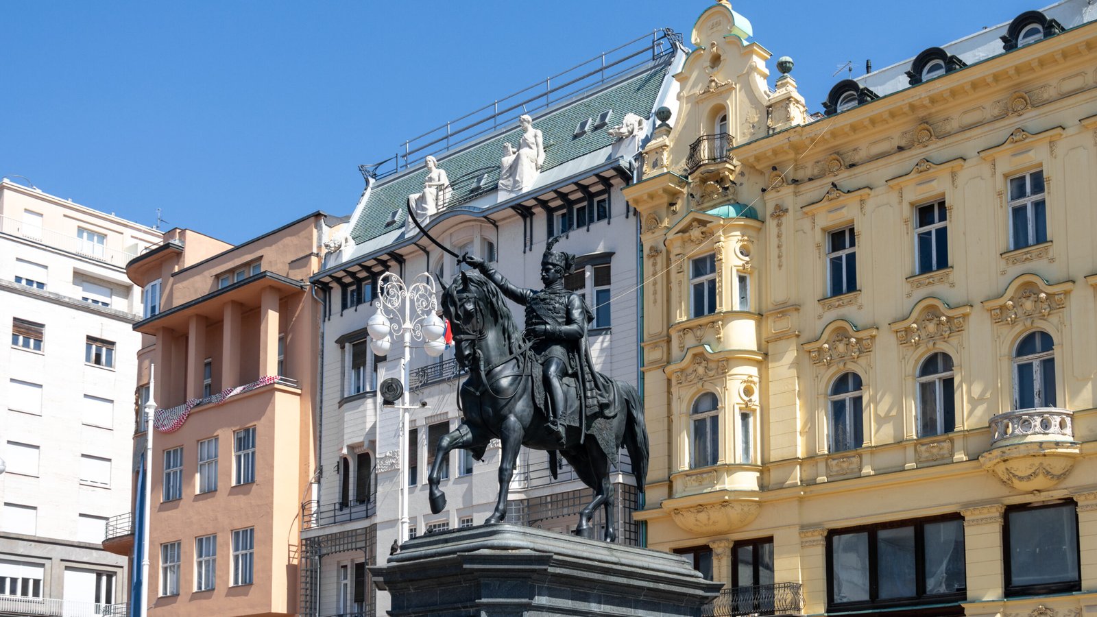 Equestrian statue in a city square with a decorative yellow building behind.