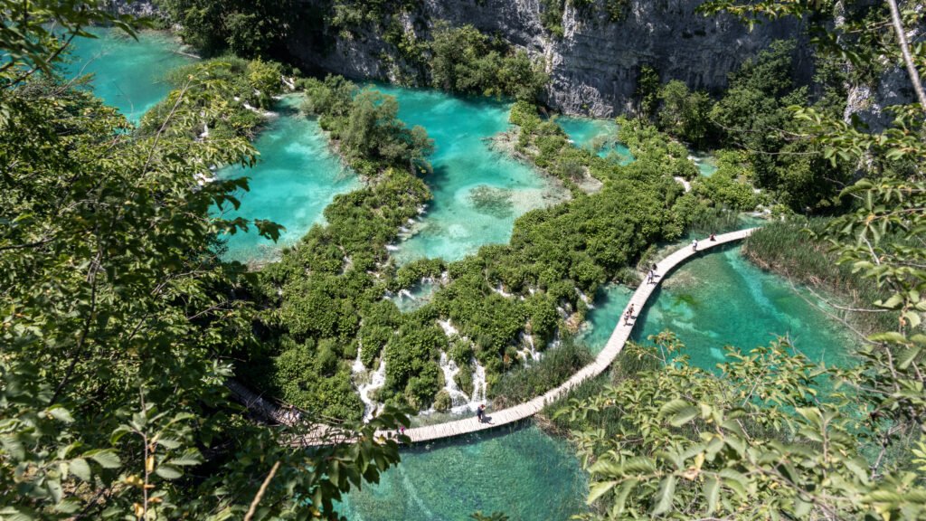 Plitvice Zagreb | Krista the Explorer Winding wooden boardwalk over turquoise river amid lush forested canyon.