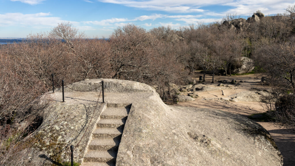 Stone stairway carved into rock, with a chain railing in forest.