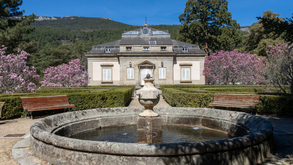 Small stone mansion with garden and water fountain in front.