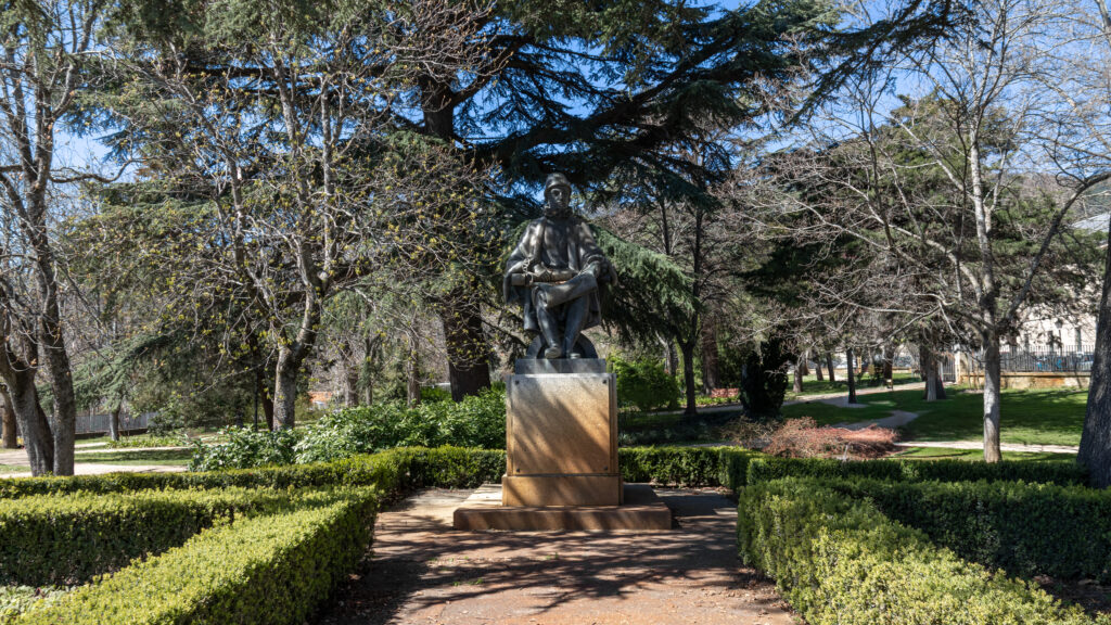 Bronze statue of a Spanish king seated in park.