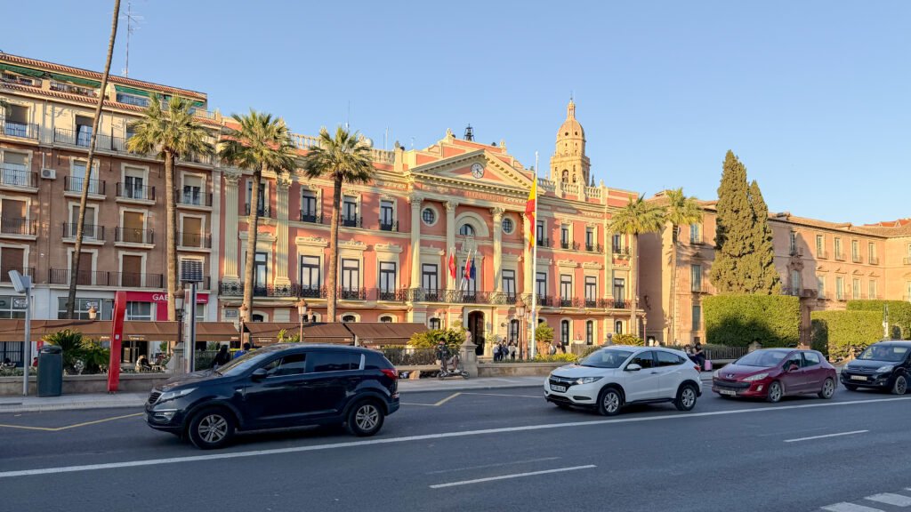 Ayuntamiento de Murcia | Krista the Explorer Facade of a pink and cream neoclassical town hall with flags.