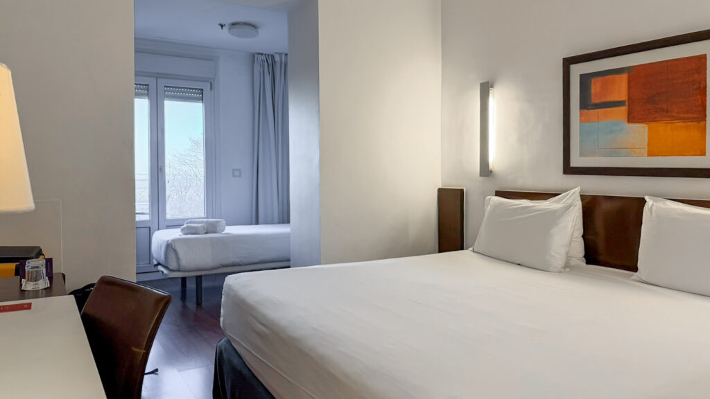Hotel bedroom with two neatly made white beds and a writing desk.
