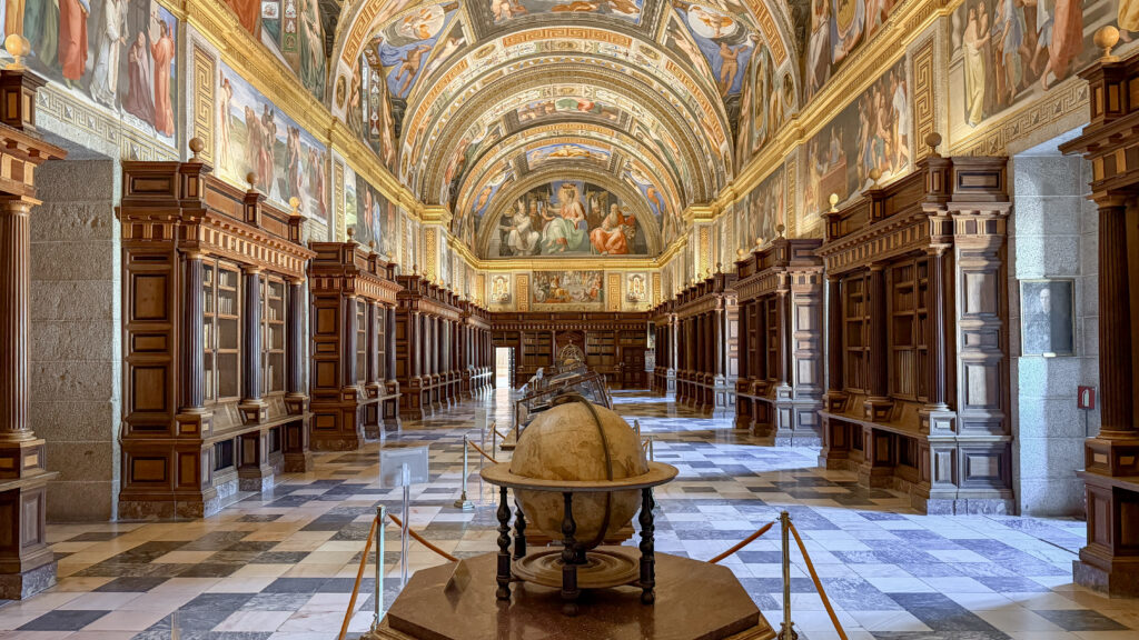 Grand library hall with ornate muralled arches, gold detailing, and tall wooden bookcases.