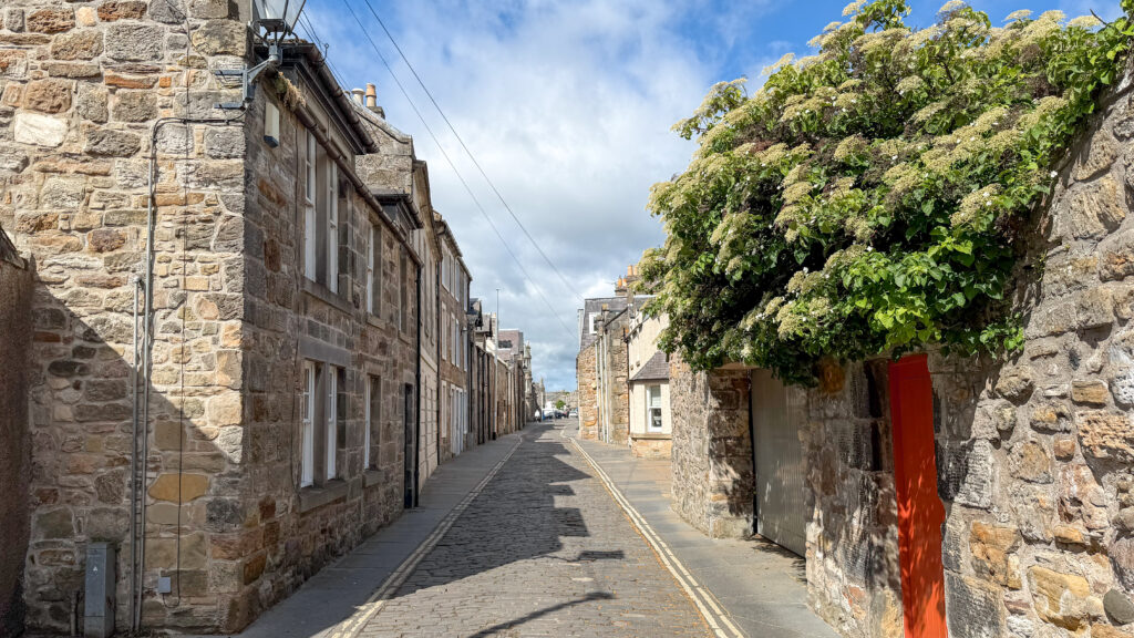 Narrow cobblestone street lined with stone houses, and a ivy-covered stone wall.