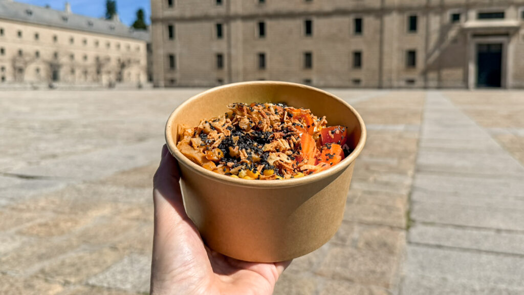 Hand holding poke bowl up in front of historic building.