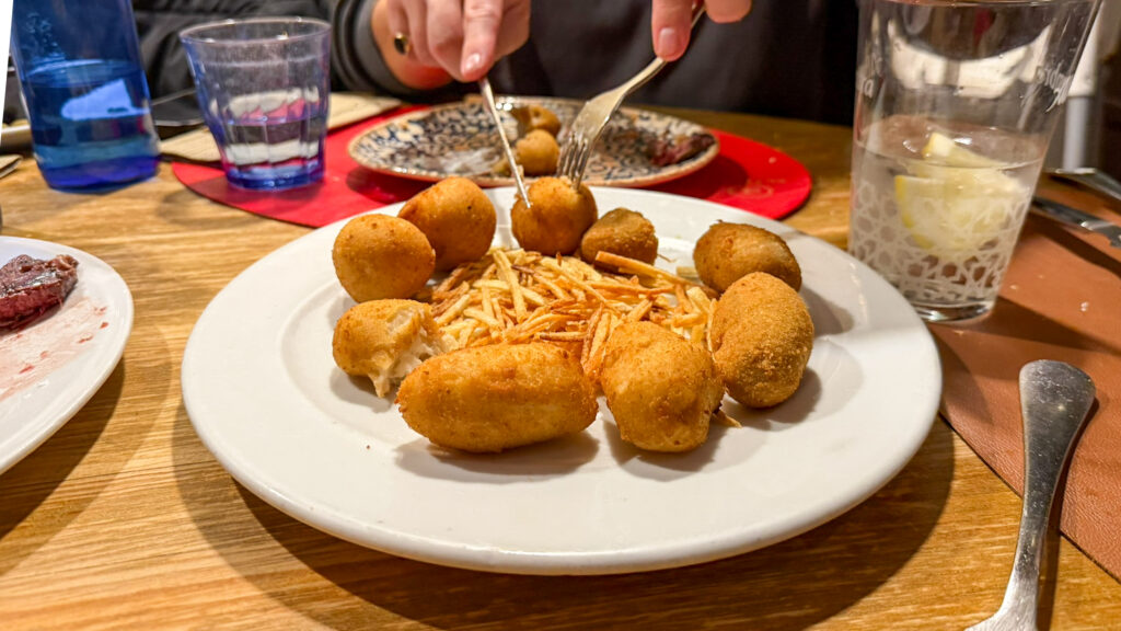 Plate of crispy croquettes arranged around shredded potato garnish.