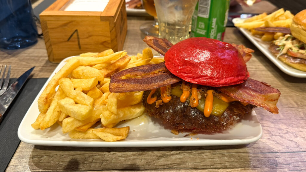 Burger with a bright red bun topped with bacon, melted cheese and jalapeños.