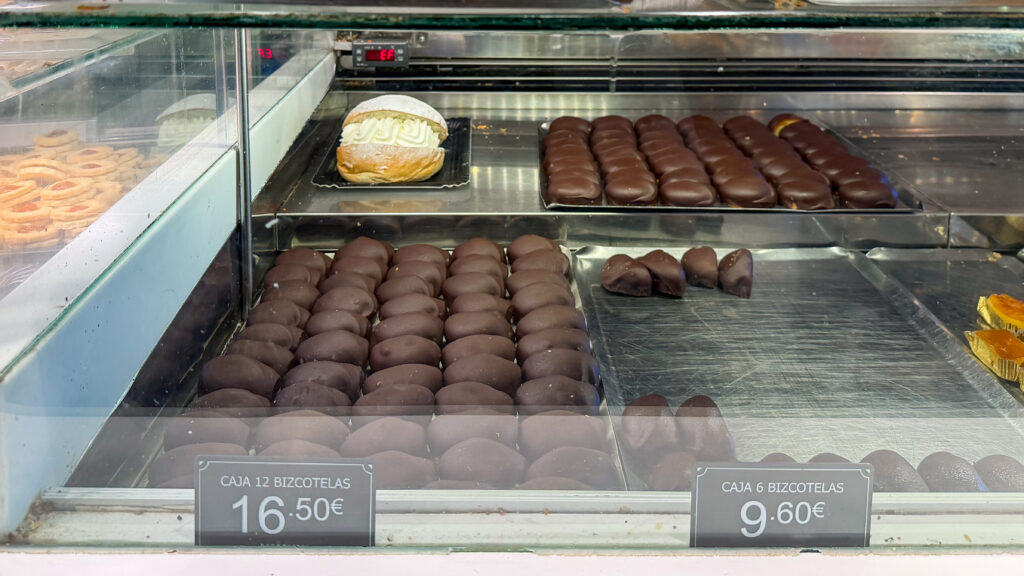 Assorted pastries in a glass bakery display, including chocolate-covered rounds and a cream-filled pastry.