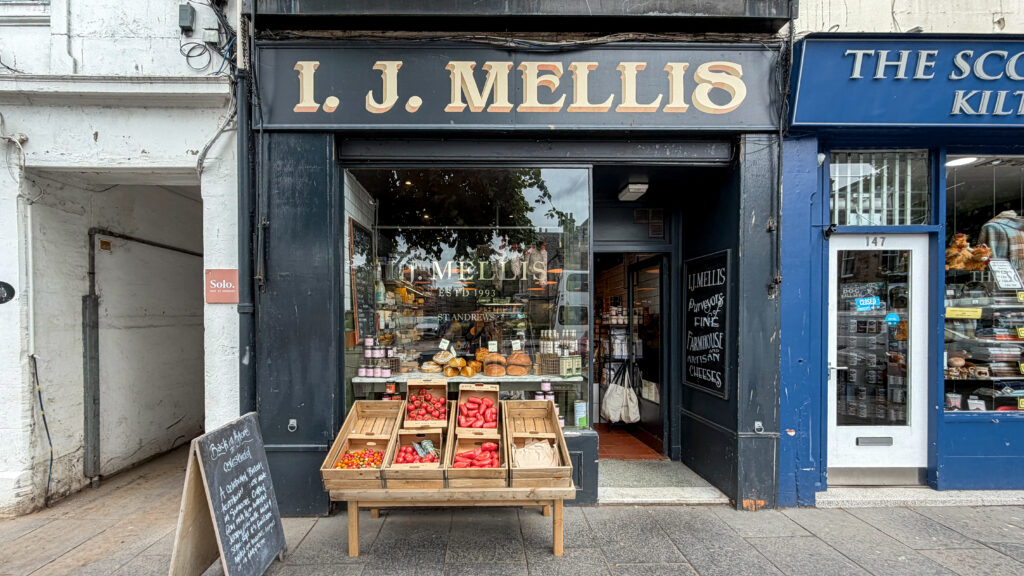 Storefront of J. Mellis Cheese with crates of produce displayed outside.