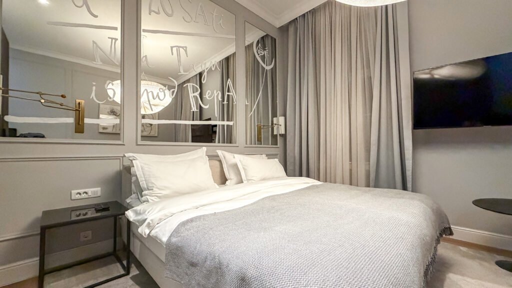 Hotel-style bedroom with two white pillows, gray bedding, and a mirrored headboard.