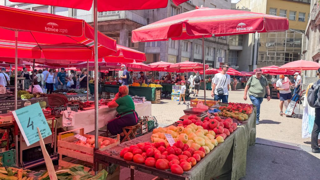 Outdoor market with red umbrellas and stalls of mixed fruit and vegetables.