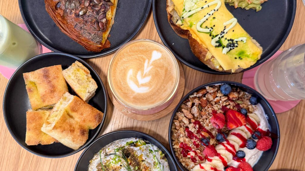 Overhead view of a brunch spread with coffee, pastries, toast, and fruit bowls.