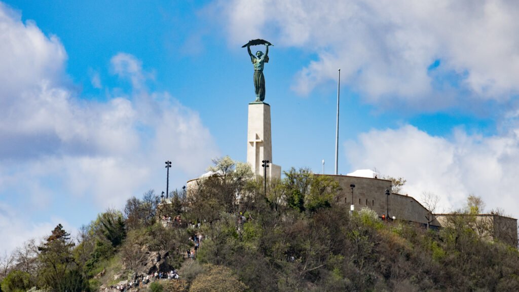Bronze statue atop a tall light-colored pedestal on a hill.