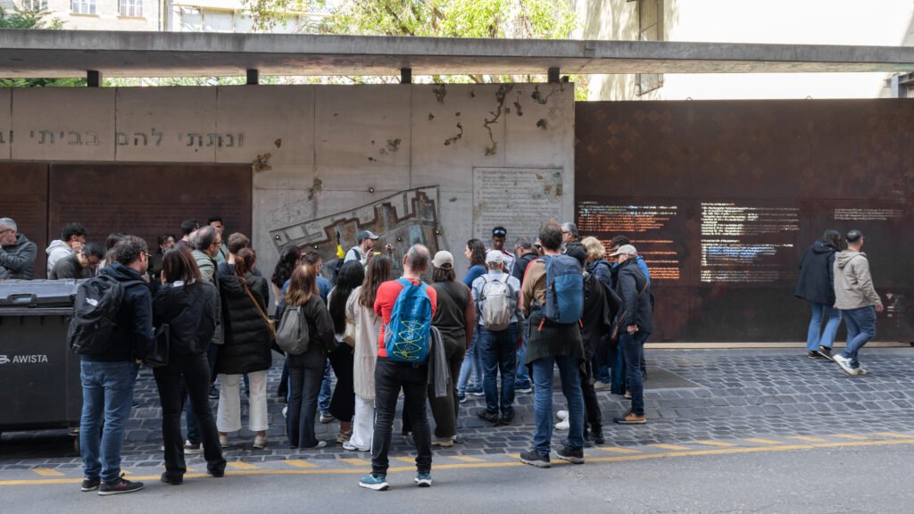 Crowd of people gathered in front of a long memorial wall.