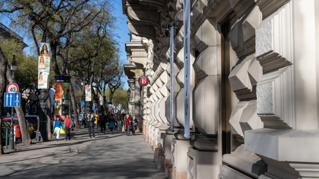 Pedestrian street lined with a large ornate beige buildings.
