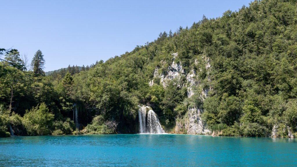 Plitvice Lakes | Krista the Explorer Turquoise lake with a multi-tier waterfall spilling from rocky cliffs.