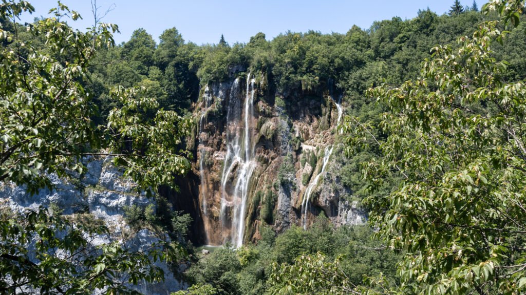 Plitvice Lakes | Krista the Explorer Waterfall cascading down a rocky cliff surrounded by dense forest.