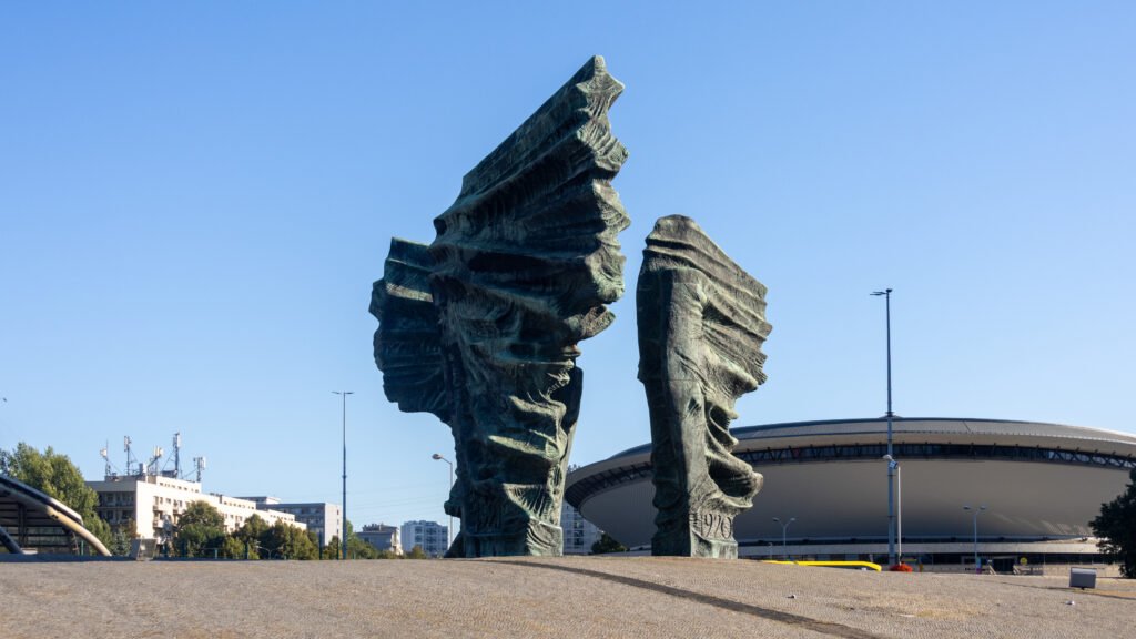 Abstract outdoor sculpture with large, weathered finger-like forms reaching upward.