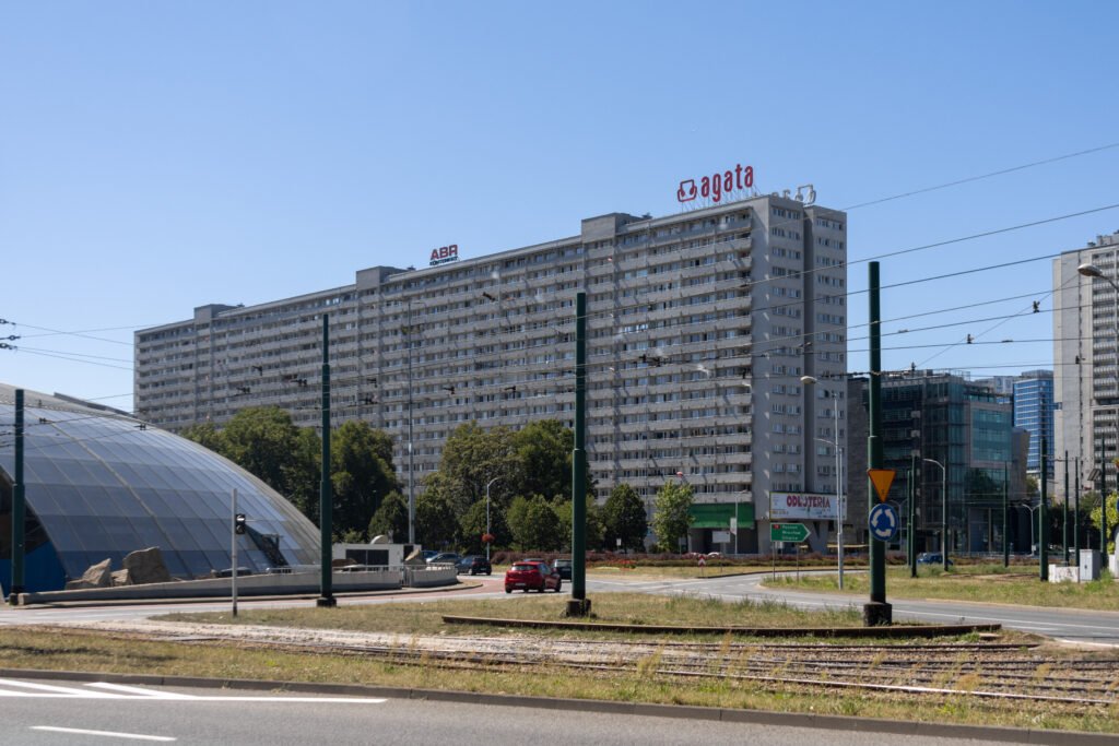 Large gray apartment building with many balconies under a clear blue sky.