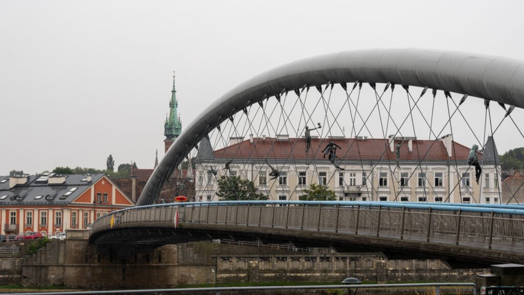 Podgorski Bridge Krakow | Krista the Explorer Suspended arch bridge with dangling sculpture figures over a river.