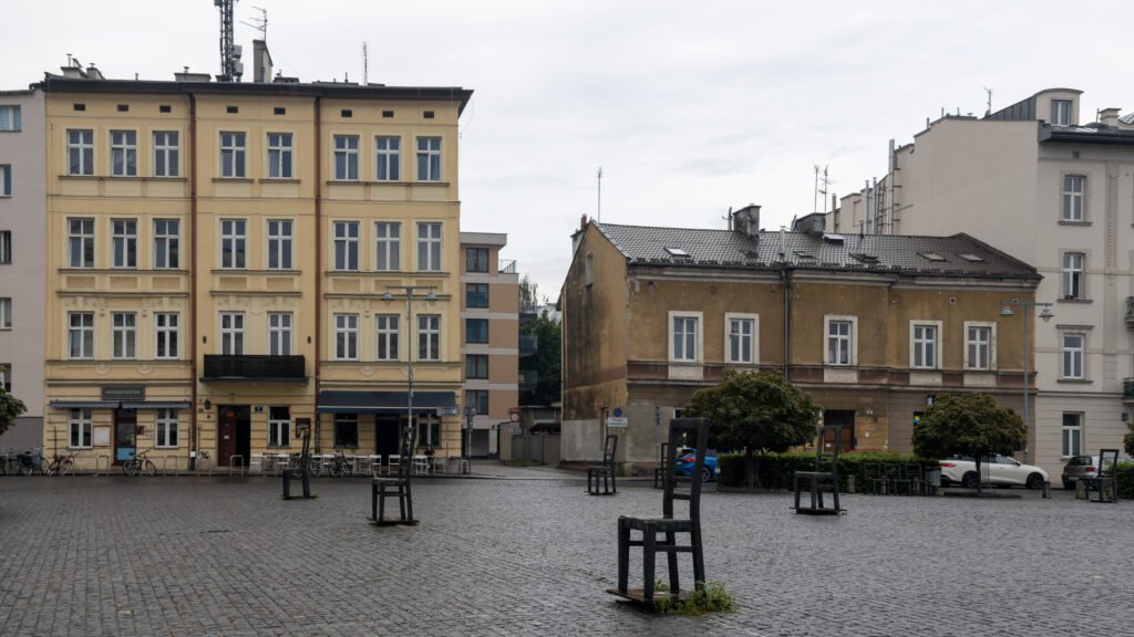 Ghetto Heroes Square Krakow | Krista the Explorer A row of old European buildings facing a cobblestone square with iron chairs placed around it.