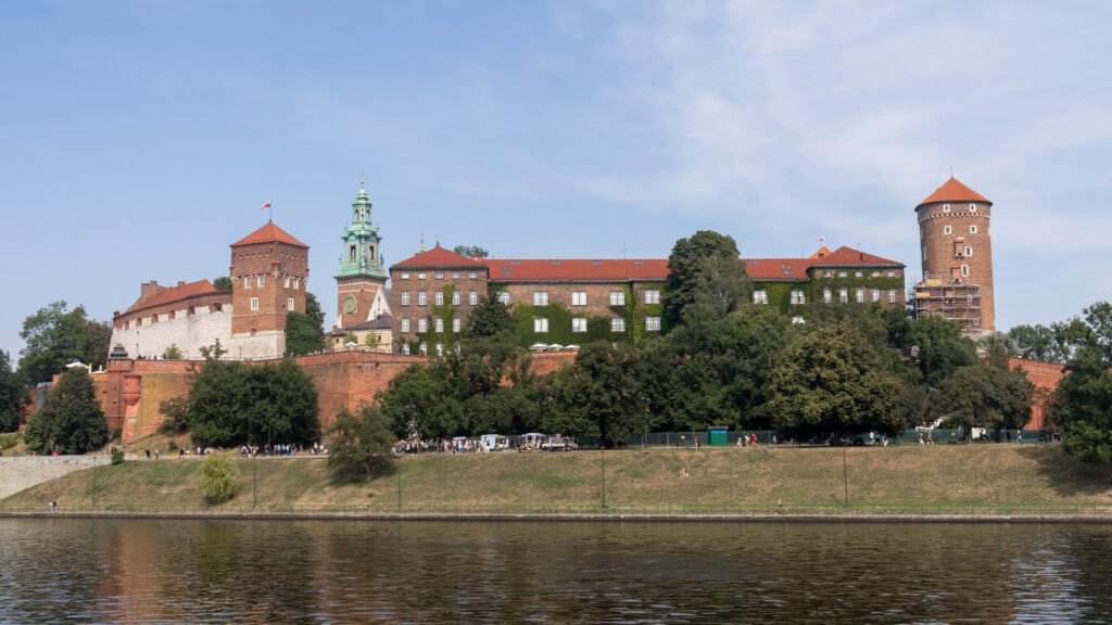 Wawel Castle Krakow | Krista the Explorer Wide view of a historic brick fortress with red-tiled roofs and rounded towers along a river.