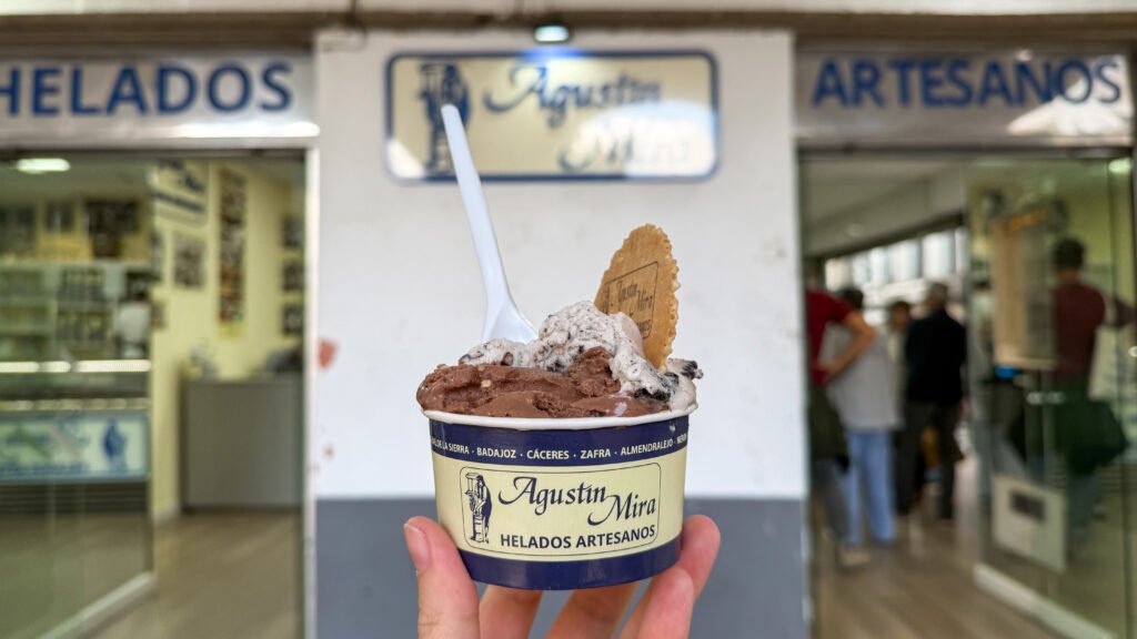 Helados Artesanos Agustin Mira Caceres | Krista the Explorer Cup of artisanal ice cream with chocolate and cookies, held up in front of a storefront.