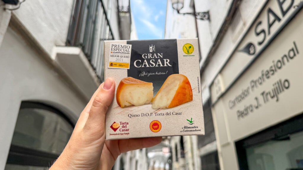 Torta del Casar Caceres | Krista the Explorer Hand holding a box of Gran Casar cheese in historic street.