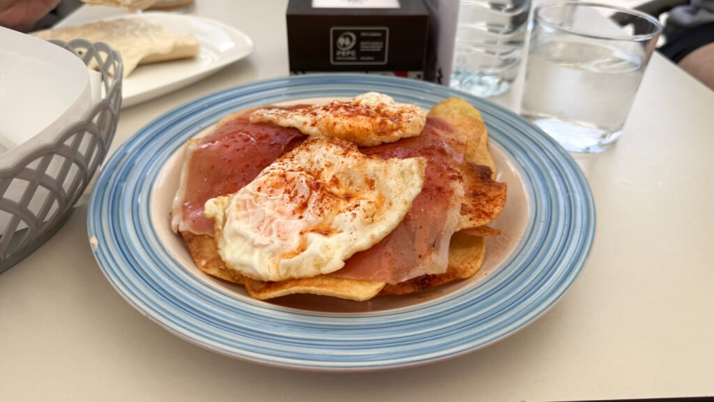 Sisters Cafe & Bar Caceres | Krista the Explorer Blue-rimmed plate with two fried eggs over sliced potatoes with jamon.