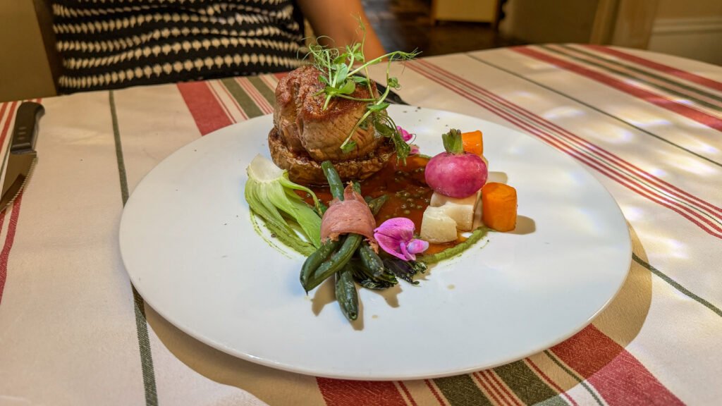 Roasted beef tenderloin with greens, carrot cubes, turnip, and green beans with sauce.