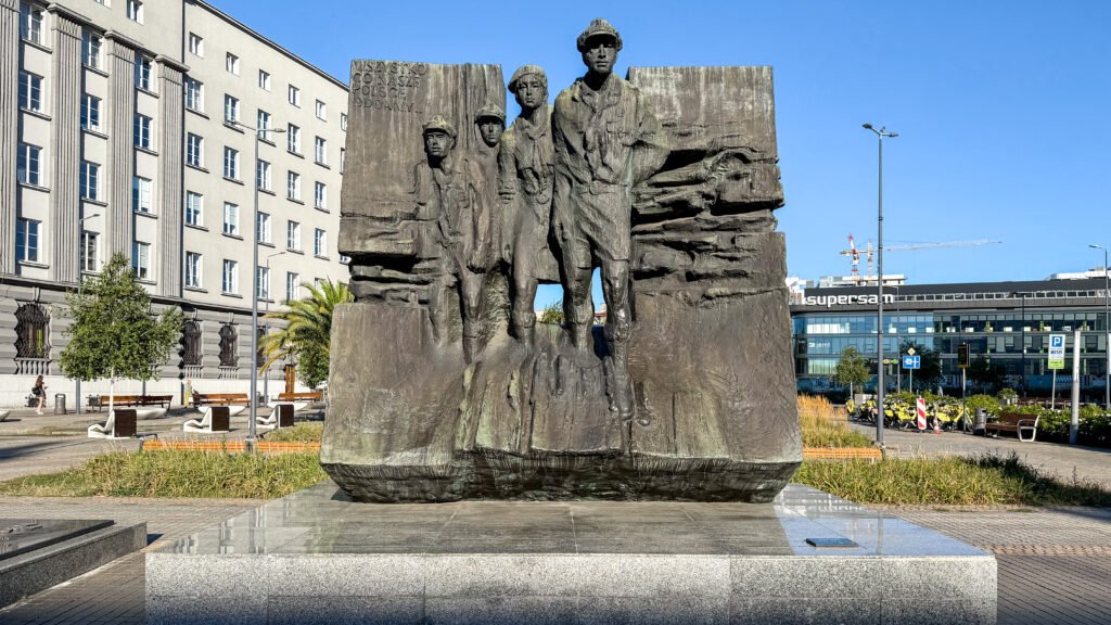 Large stone memorial sculpture of five soldiers in an urban plaza.