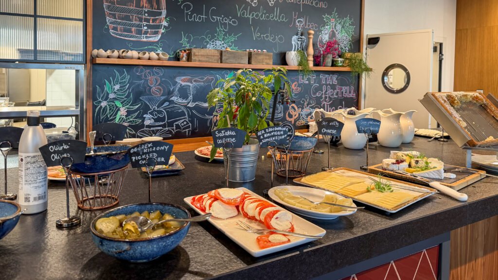 Buffet counter with cheese plates, olives, peppers, and chalkboard labels.
