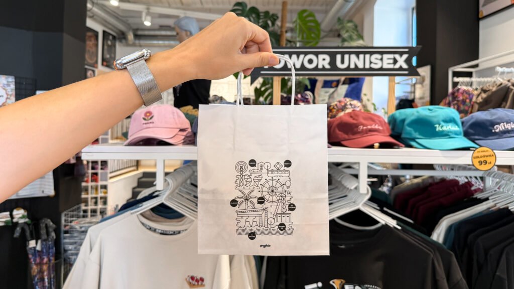 Person holds up a white shopping bag with a black graphic design inside a clothing store.