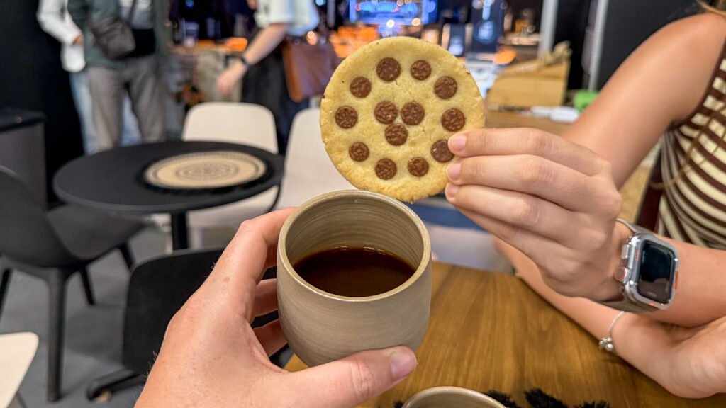 Two people share a chocolate chip cookie and a cup of coffee in a busy cafe.