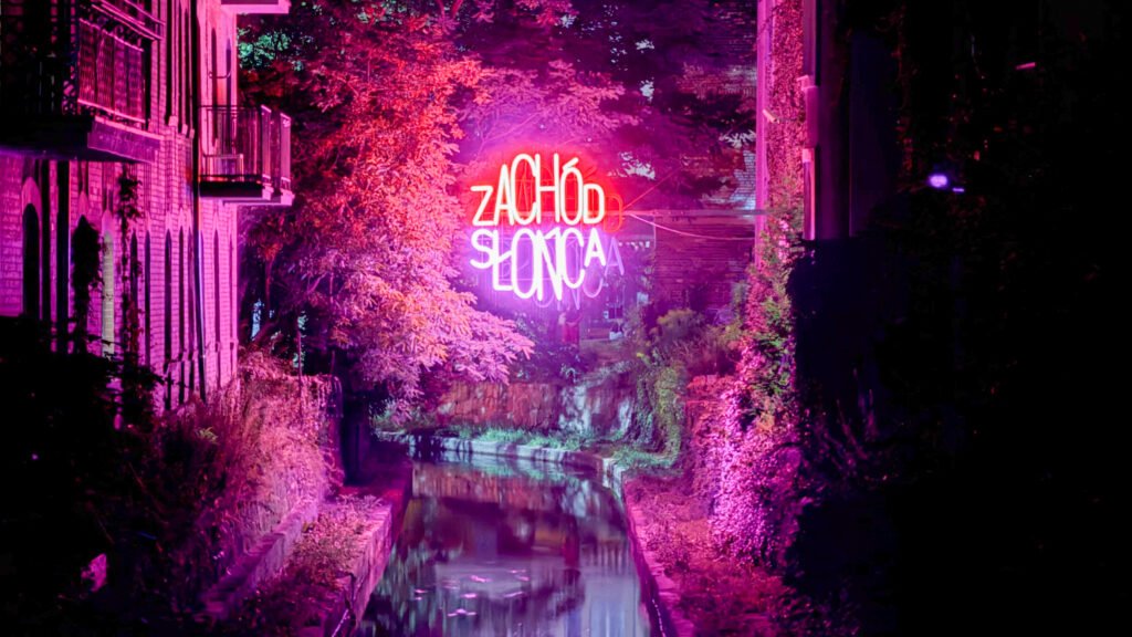 Nighttime canal scene with bright pink neon sign over the water.