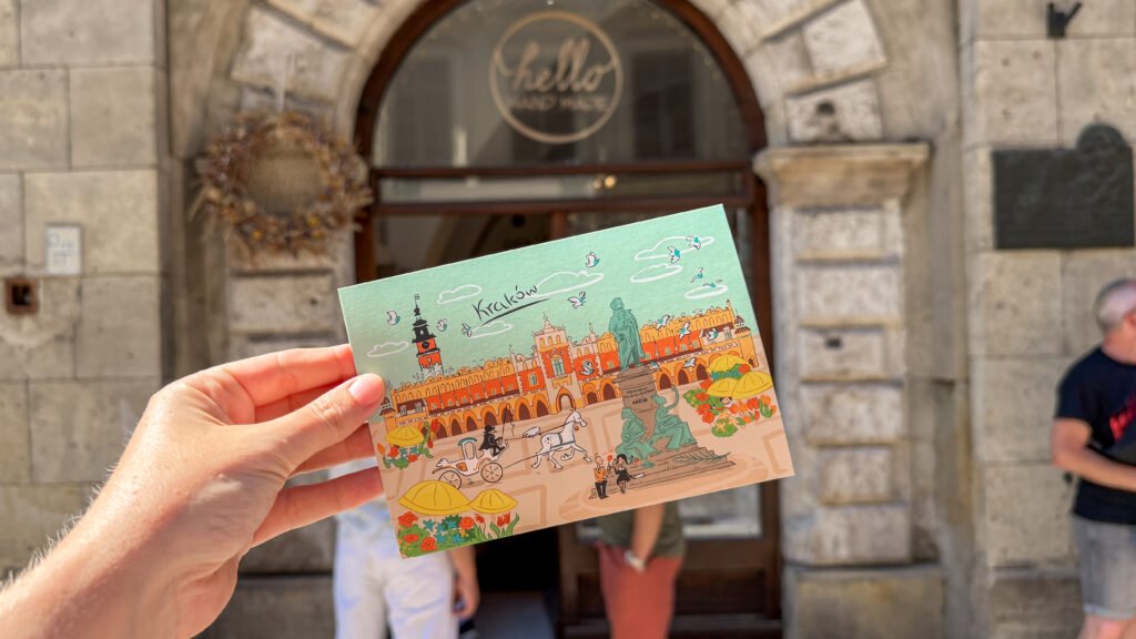 Hello Handmade Krakow | Krista the Explorer Hand holding a colorful Kraków illustration postcard in front of a historic stone arch doorway.