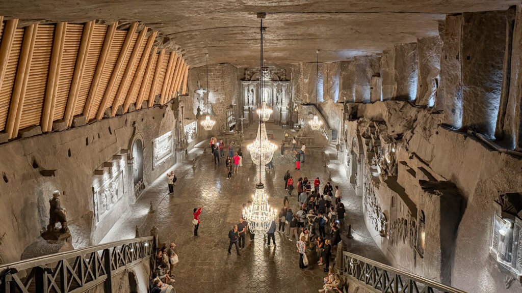 Wieliczka Salt Mine Krakow | Krista the Explorer Underground chapel with stone walls, large chandeliers, and visitors touring the vaulted hall.