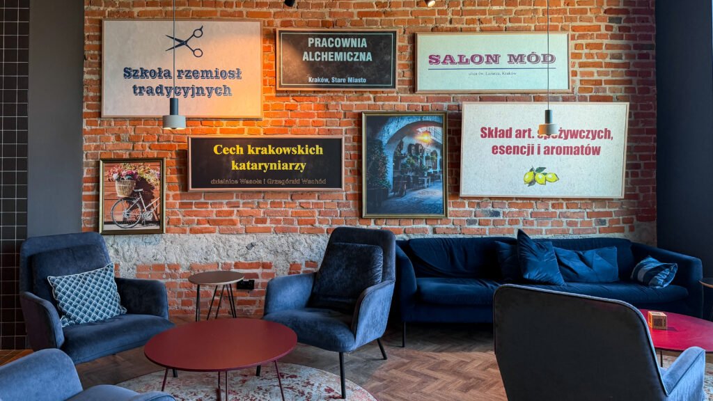 MEININGER Kraków Centrum | Krista the Explorer Cozy seating area with blue sofas against a red brick wall and framed wall art in Polish above.