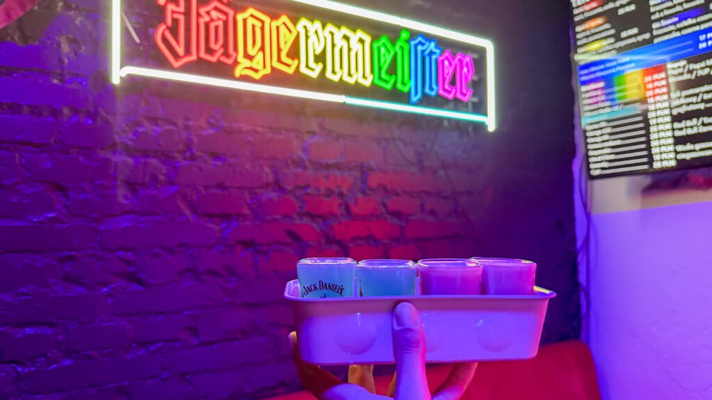 Lindo Bar Krakow | Krista the Explorer Bar scene with a multicolor neon sign on a brick wall and a server holding a tray of bright drinks.