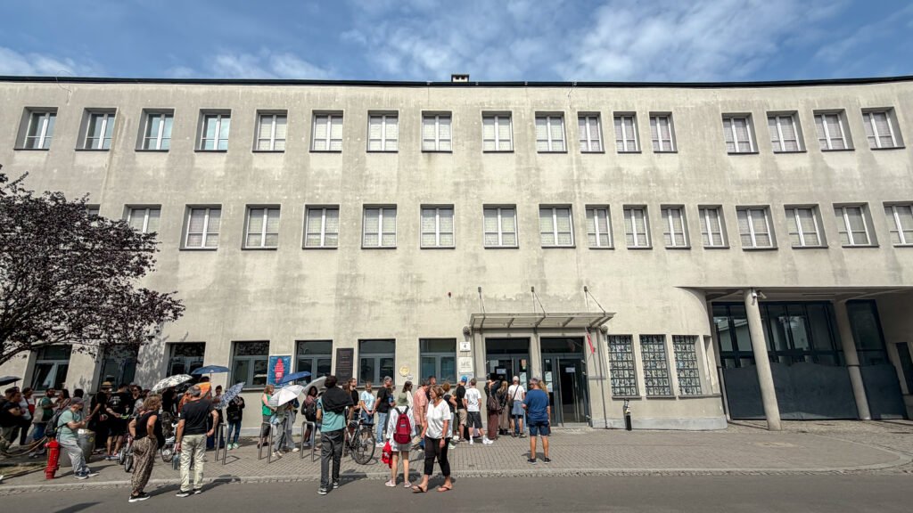 Oskar Schindler's Enamel Factory Krakow | Krista the Explorer Line of people with umbrellas outside a gray, multi-story building with many windows.