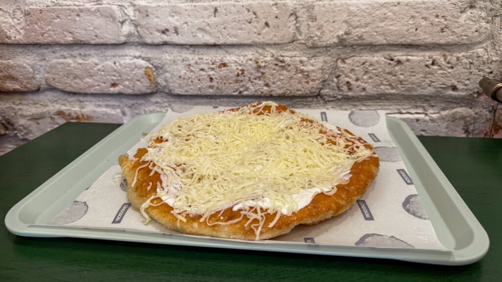 Langos topped with sour cream and shredded cheese.