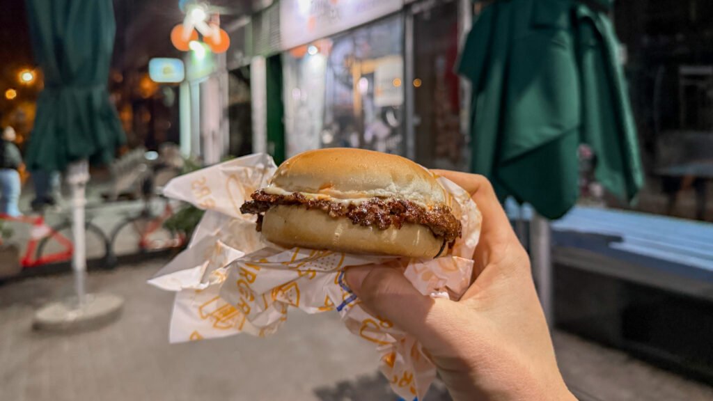 Hand holding a smash burger on the street at night.