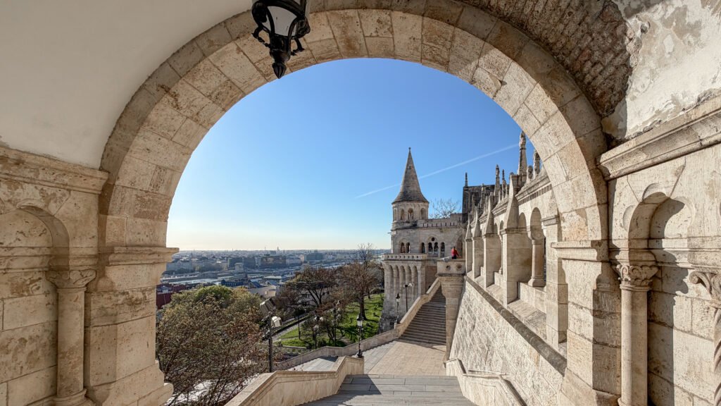 Stone archway framing a terrace with a spired tower and distant city.